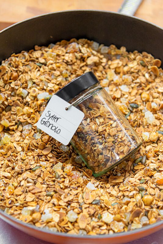 Ein umgekipptes Glas Sylter Manufaktur Leichtes Gourmet-Frühstücks-Müsli auf einem Backblech, mit der Aufschrift „Zuckermüsli“.