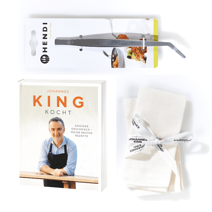 Eine Reihe von Küchenutensilien, ordentlich arrangiert auf weißem Hintergrund, darunter in der Verpackung oben ein Geschenk für Kochbegeisterte der Sylter Manufaktur, ein gebundenes Kochbuch mit einem lächelnden Mann und dem Titel „Johannes King“.