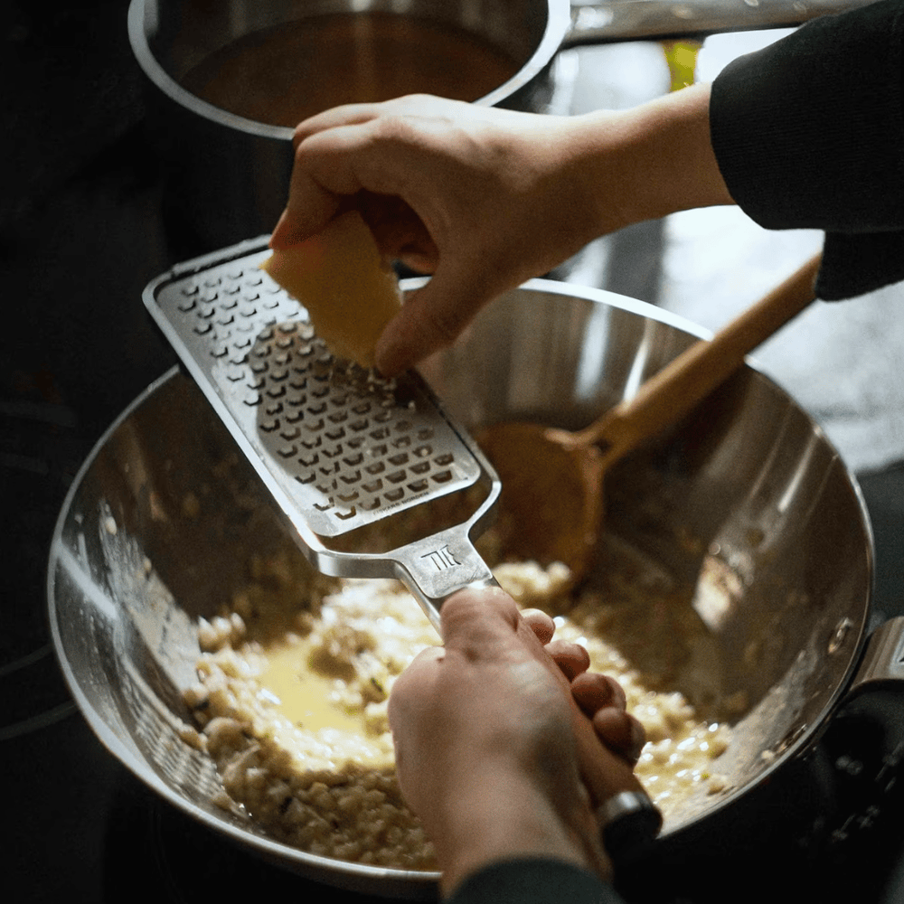 Eine Person reibt beim Kochen mit einer Fiskars Norden Handreibe grob der Fiskars Group Käse in eine Schüssel mit Zutaten.