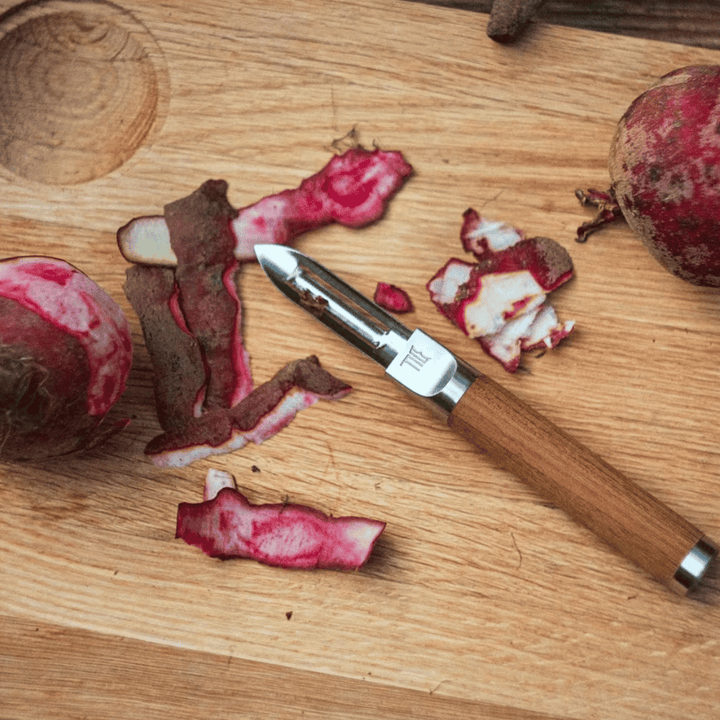 Ein Fiskars Norden Schäler liegt neben geschälten und teilweise geschnittenen Granatäpfeln auf einem Holzschneidebrett.