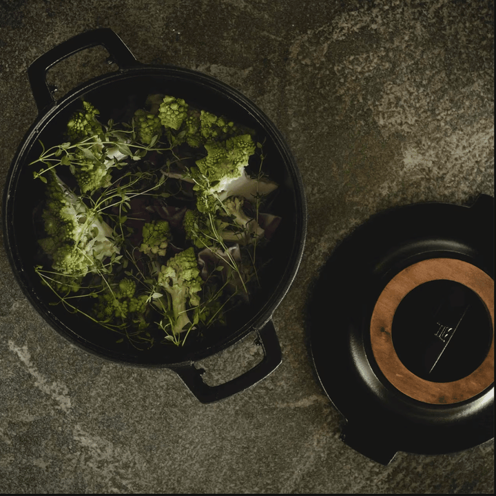 Ein Fiskars Norden Topf 4,0 l gefüllt mit rohem grünem Gemüse und Kräutern auf einem dunklen Untergrund, daneben liegt der Deckel.