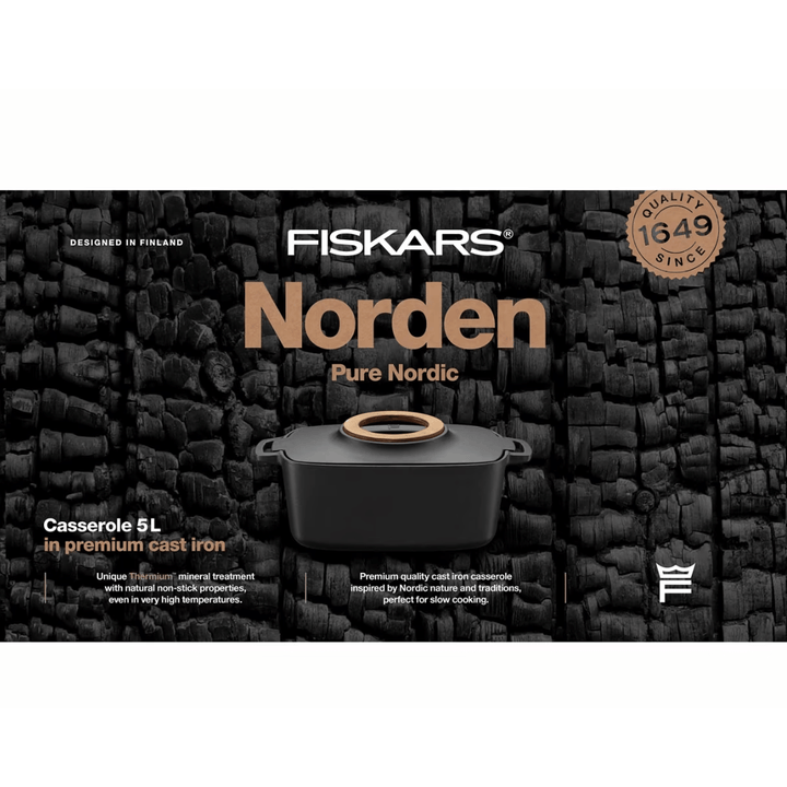 Ein ovaler Gusseisentopf von Fiskars Norden Topf mit 5,0 l Fassungsvermögen vor einem dunklen Hintergrund aus Holzstapeln, der die Qualität und das Erbe des nordischen Designs des Kochgeschirrs hervorhebt.