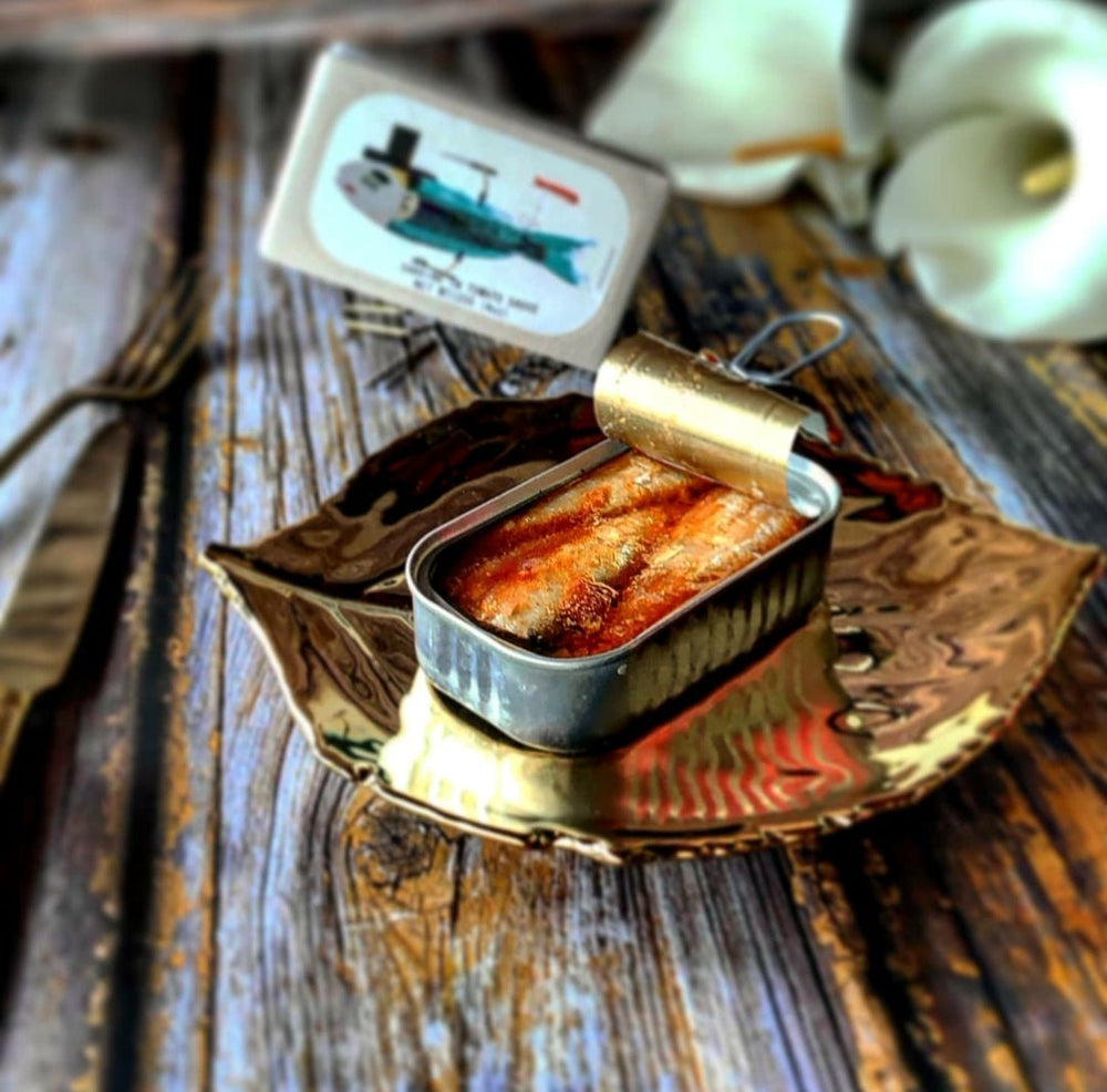 Eine geöffnete Dose Jose Gourmet Sardinen in Tomatensauce ruht auf einem verzierten Teller mit einer Gabel daneben und teilweise geschlossenem Deckel.