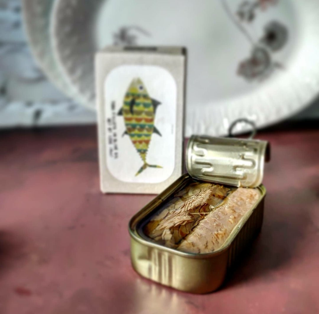 Eine geöffnete Dose Jose Gourmet Thunfischfilets in Olivenöl steht mit teilweise geschlossenem Deckel auf einem Tisch, neben einer illustrierten Fischkarte.