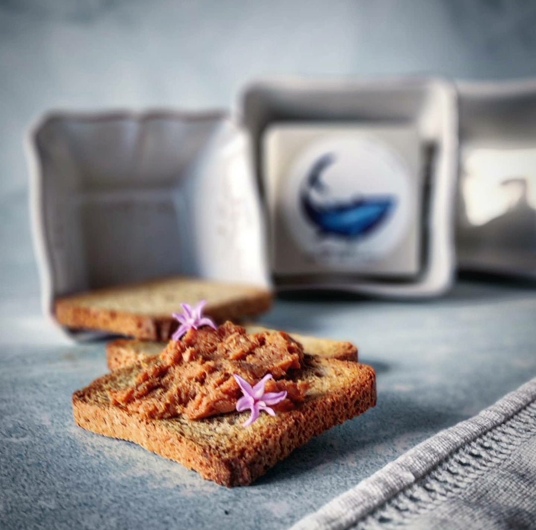 Knusprige Toastscheiben mit Blumengarnitur, begleitet von einer Butterdose und Jose Gourmet Thunfisch Mousse, auf einer strukturierten Oberfläche.