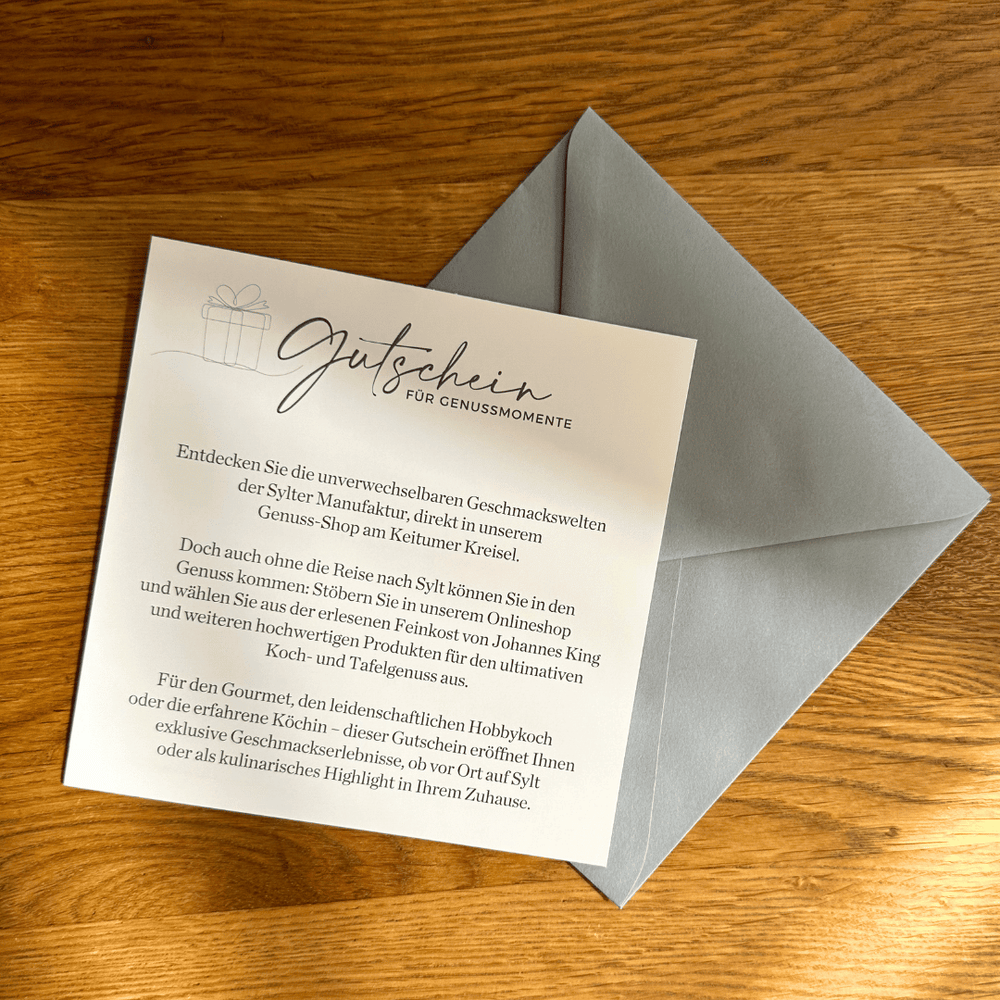 Ein Geschenkgutschein von Johannes King für Gourmet-Momente neben einem grauen Umschlag auf einer Holzunterlage.