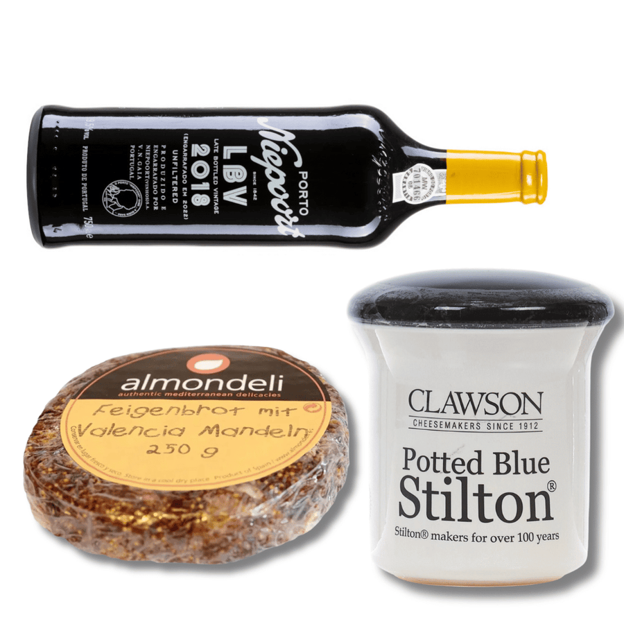 Eine Auswahl an Gourmet-Lebensmitteln, darunter eine Flasche Kleines Portwein-Set von der Sylter Manufaktur, ein Behälter mit blauem Stilton-Käse im Topf und eine Packung Früchtebrot mit Valencia-Mandeln.
