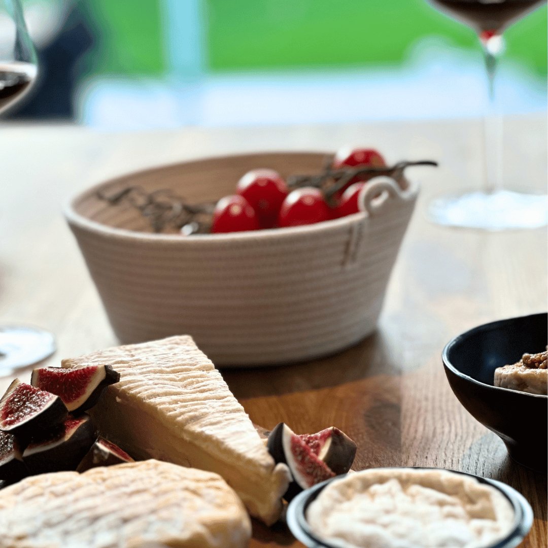 Eine Auswahl an Vorspeisen, darunter Käse, Feigen und Tomaten, auf einem Holztisch mit einem Glas Rotwein im Hintergrund, präsentiert in Mia Mélange Baumwollkorb, klein (D 15 cm x H 5 cm) Schalen.