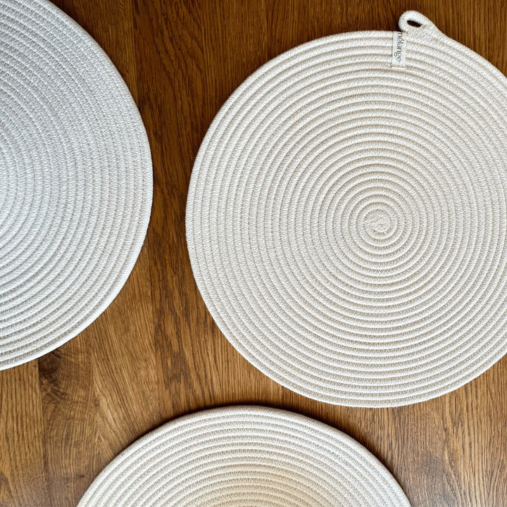 Drei runde, handgefertigte Mia Mélange Baumwoll-Tischsets (32 cm) unterschiedlicher Größe auf einem Holzboden angeordnet.