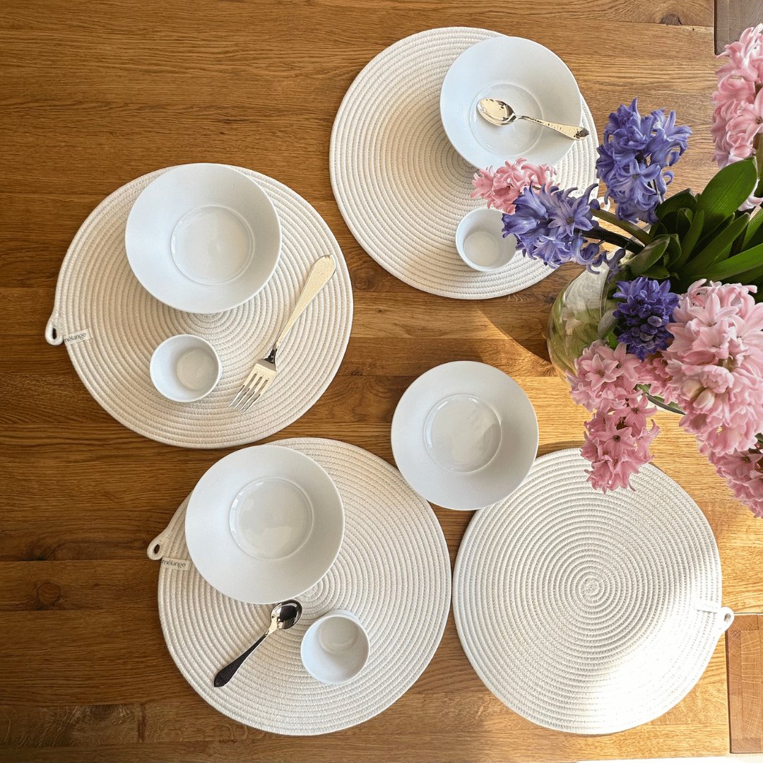 Ein hübsch arrangierter Esstisch für vier Personen mit Mia Mélange Baumwoll-Tischsets (32cm), schlichtem weißem Geschirr, silbernem Besteck und einer Glasvase mit rosa und lila Hy