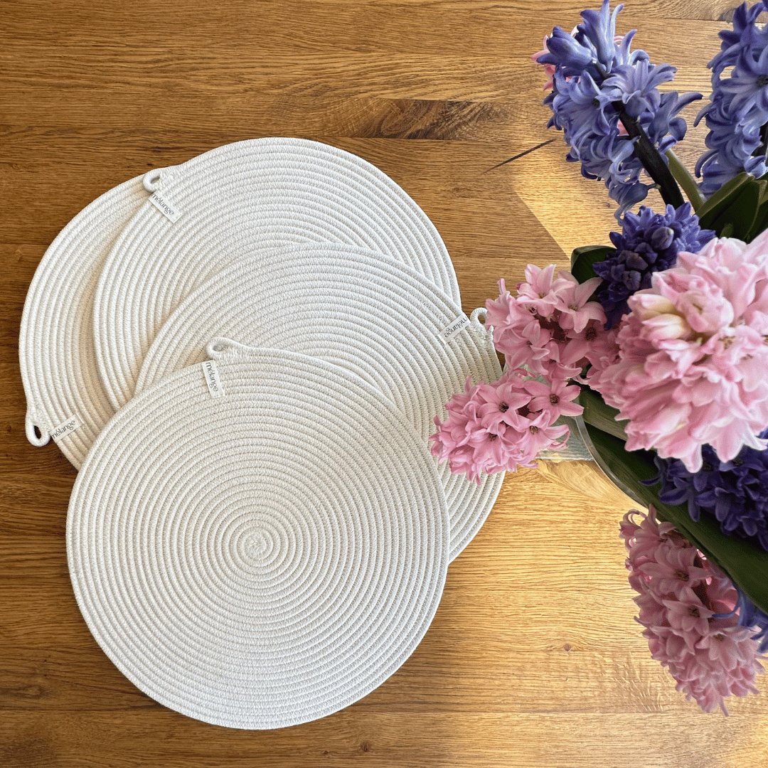Weiße Mia Mélange Baumwoll-Tischsets (32 cm), arrangiert auf einem Holztisch neben einem Strauß rosa und lila Hyazinthen.