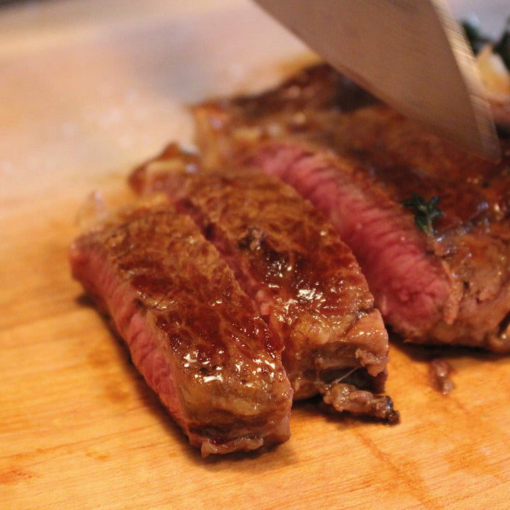 Auf einem Holzbrett mit einem Messer geschnittenes medium-rare Steak, serviert mit Kings Nussbutter von der Sylter Manufaktur.
