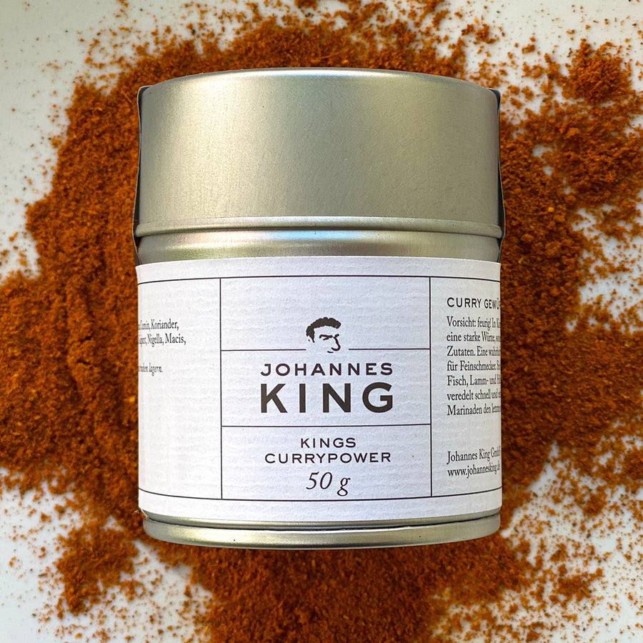 Ein Glas „Sylter Manufaktur Kings Currypower“ mit 50g Produkt umgeben von verschüttetem Currypulver auf einer Oberfläche mit exotischer Note.